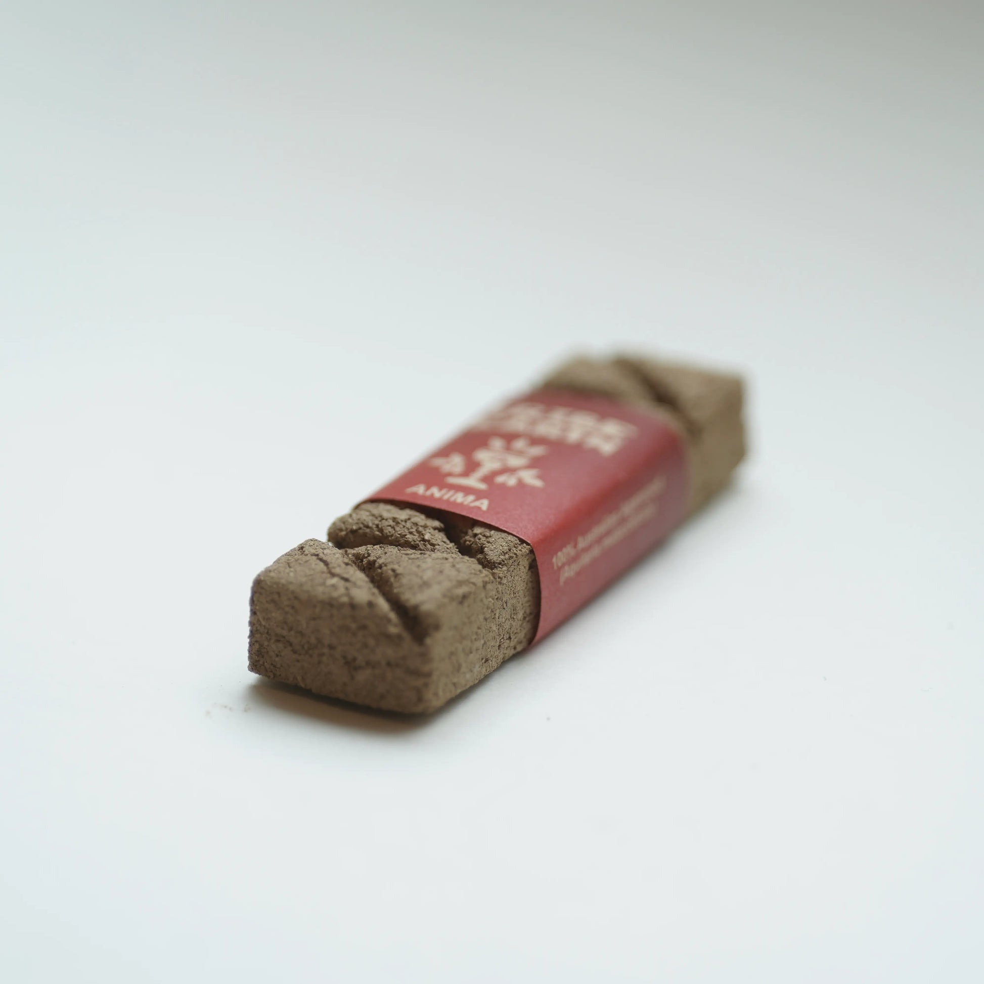 A Tribe earth anima incense wrapped in a red paper band, photographed on a clean white background.