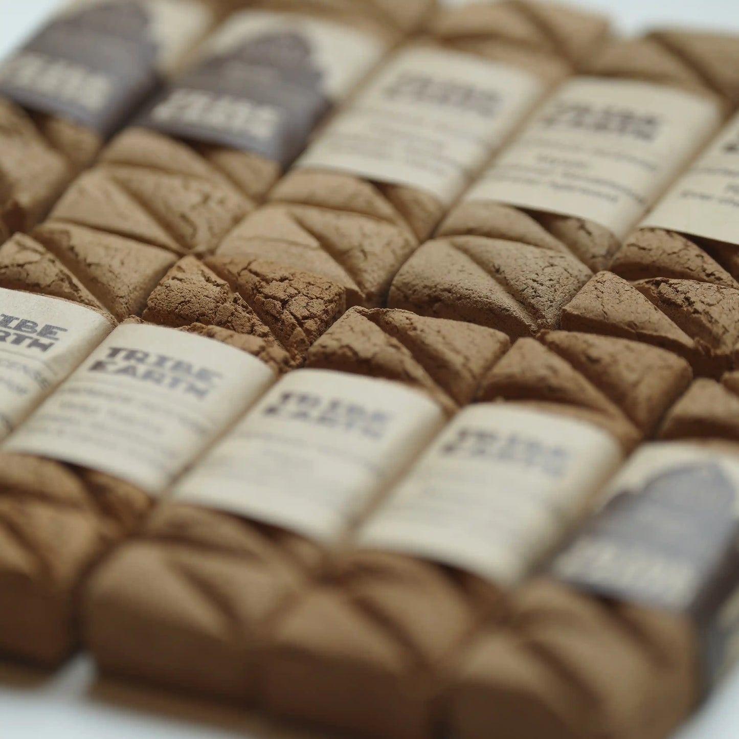 A close-up, angled view of tribe earth incenses arranged in rows. Each bar has a cream paper label wrapped around it with the brand name 'TRIBE EARTH' printed on it.