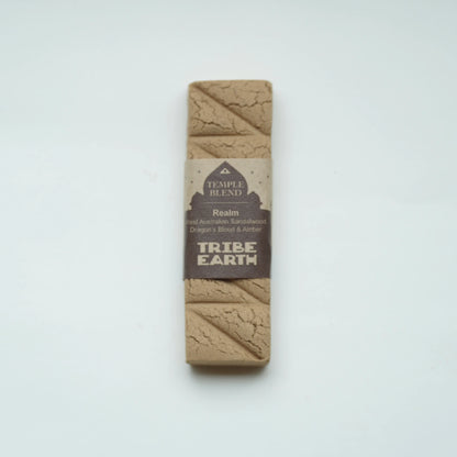 A rectangular Temple Blend Tribe Earth dog toy made of natural earth-toned material, wrapped in a brown paper band label, centered on a plain white background.