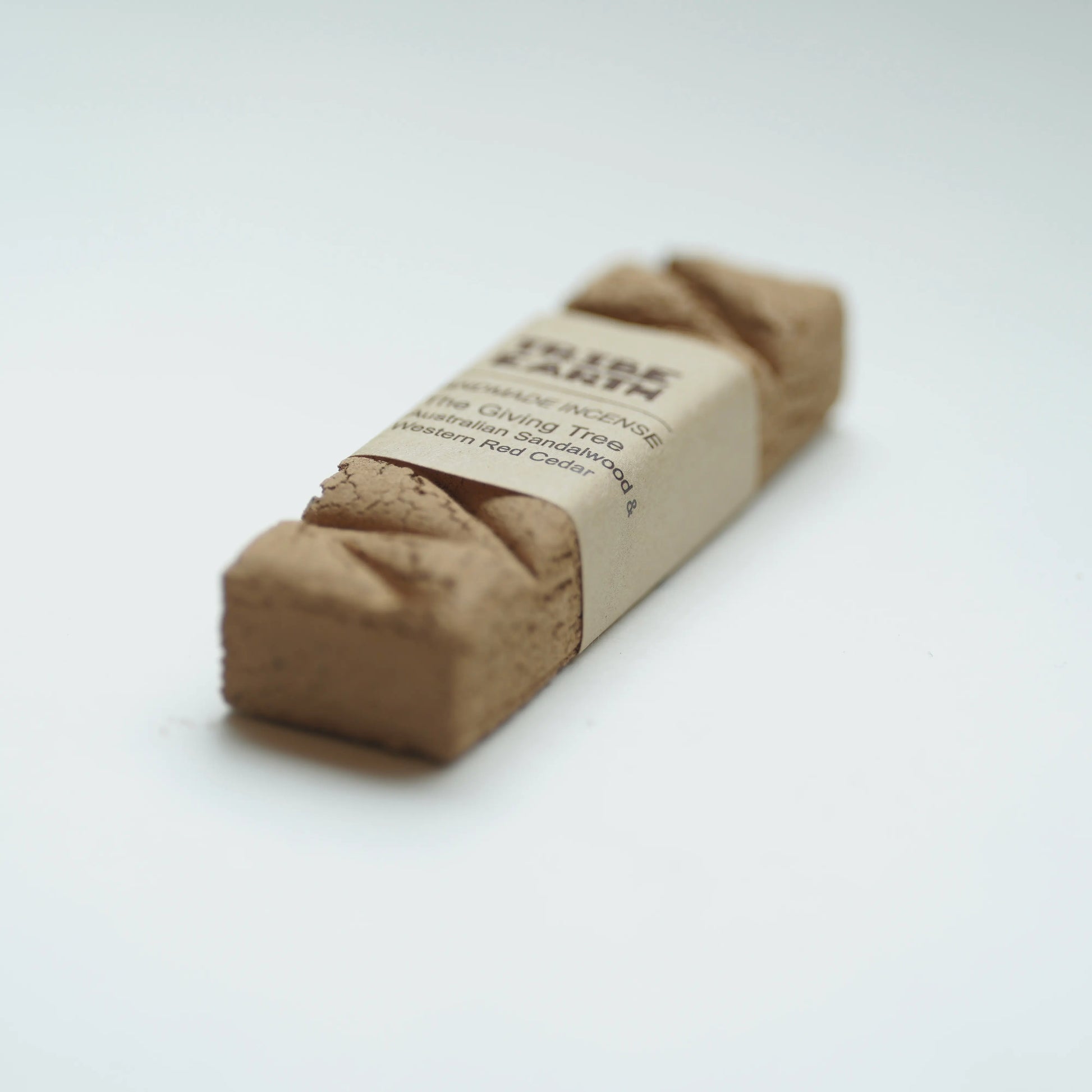 A single cube of tribe earth giving tree natural incense wrapped in a kraft paper band, photographed on a clean white background.