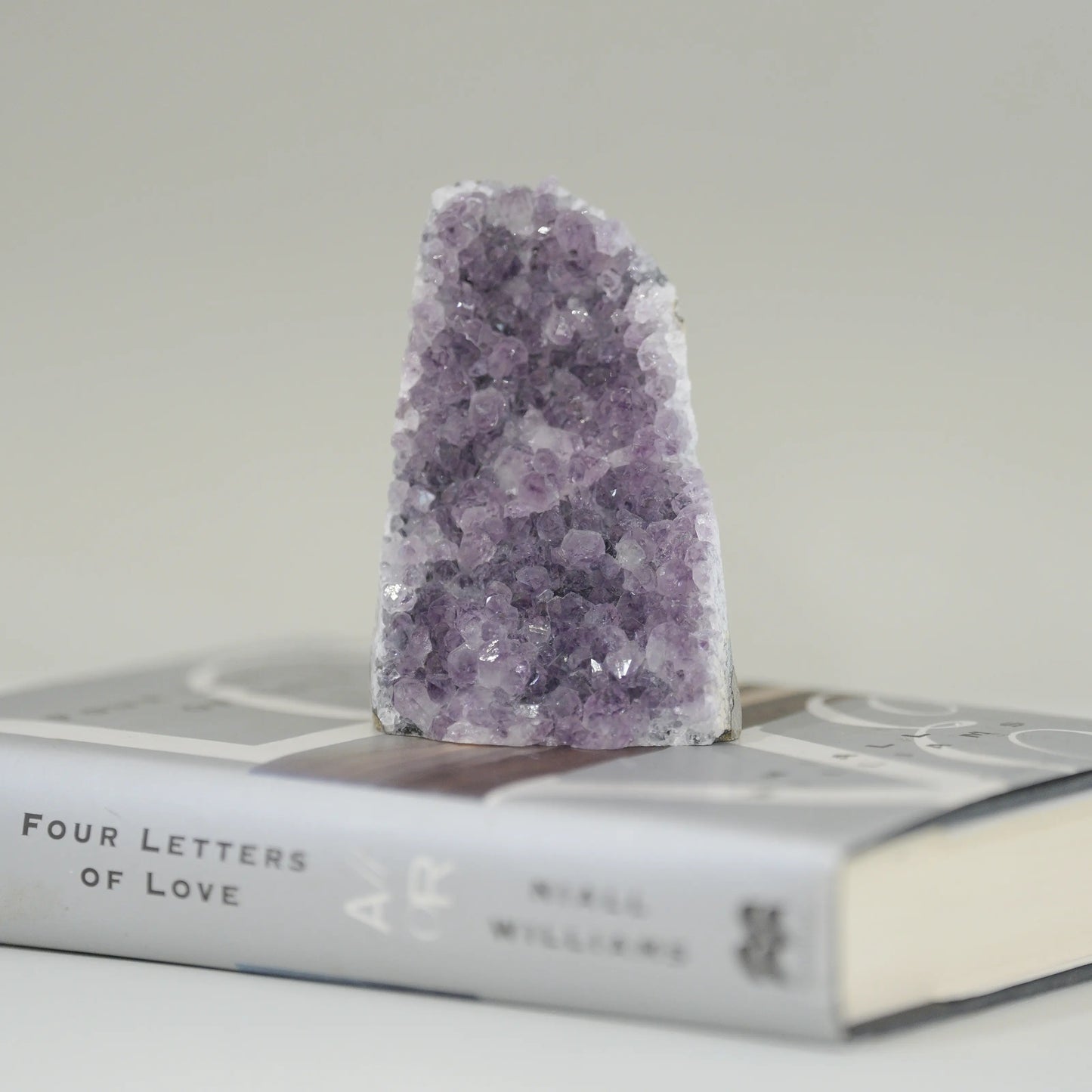 Amethyst crystal geode standing upright on a closed book titled "Four Letters of Love" by Nikki Williams.