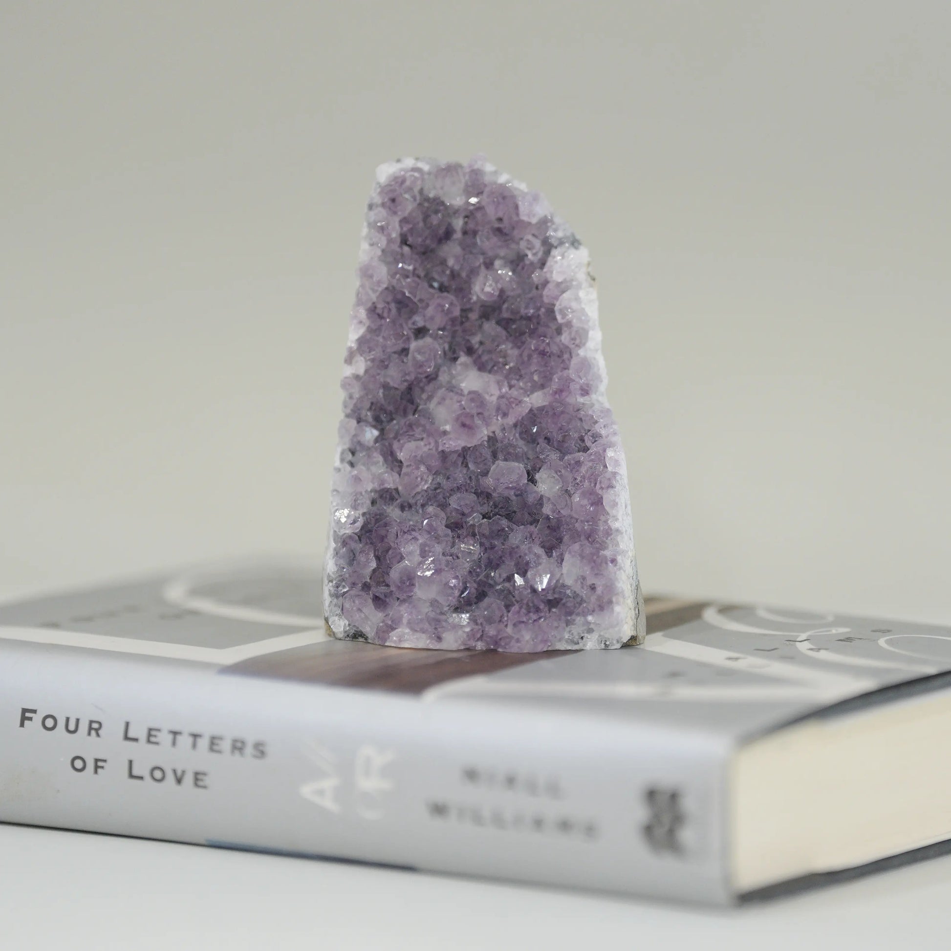 Amethyst crystal geode standing upright on a closed book titled "Four Letters of Love" by Nikki Williams.
