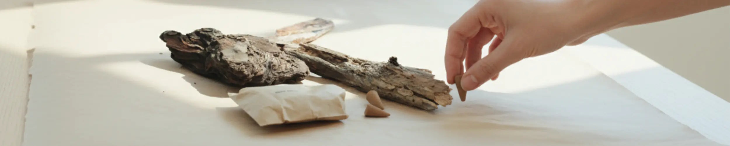 A hand carefully examines natural materials, including driftwood and small clay pieces, displayed on a light surface.