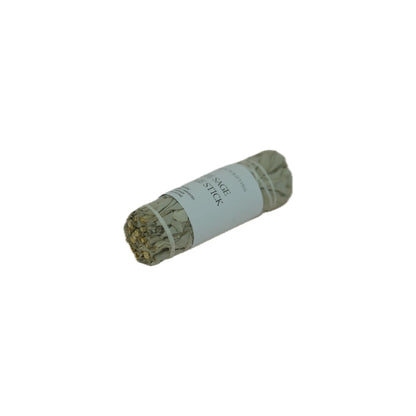 A single dried herb smudge stick wrapped in a white paper band labeled 'SAGE STICK' on a plain white background.