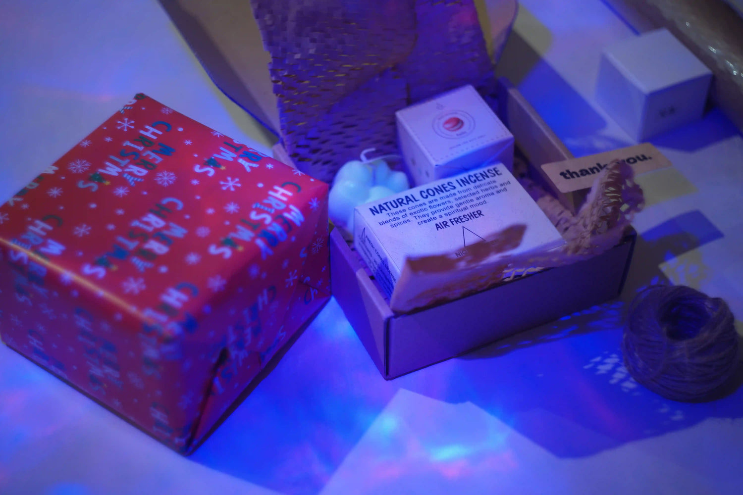 Box with Christmas-themed gift wrap and a candle on a reflective surface.