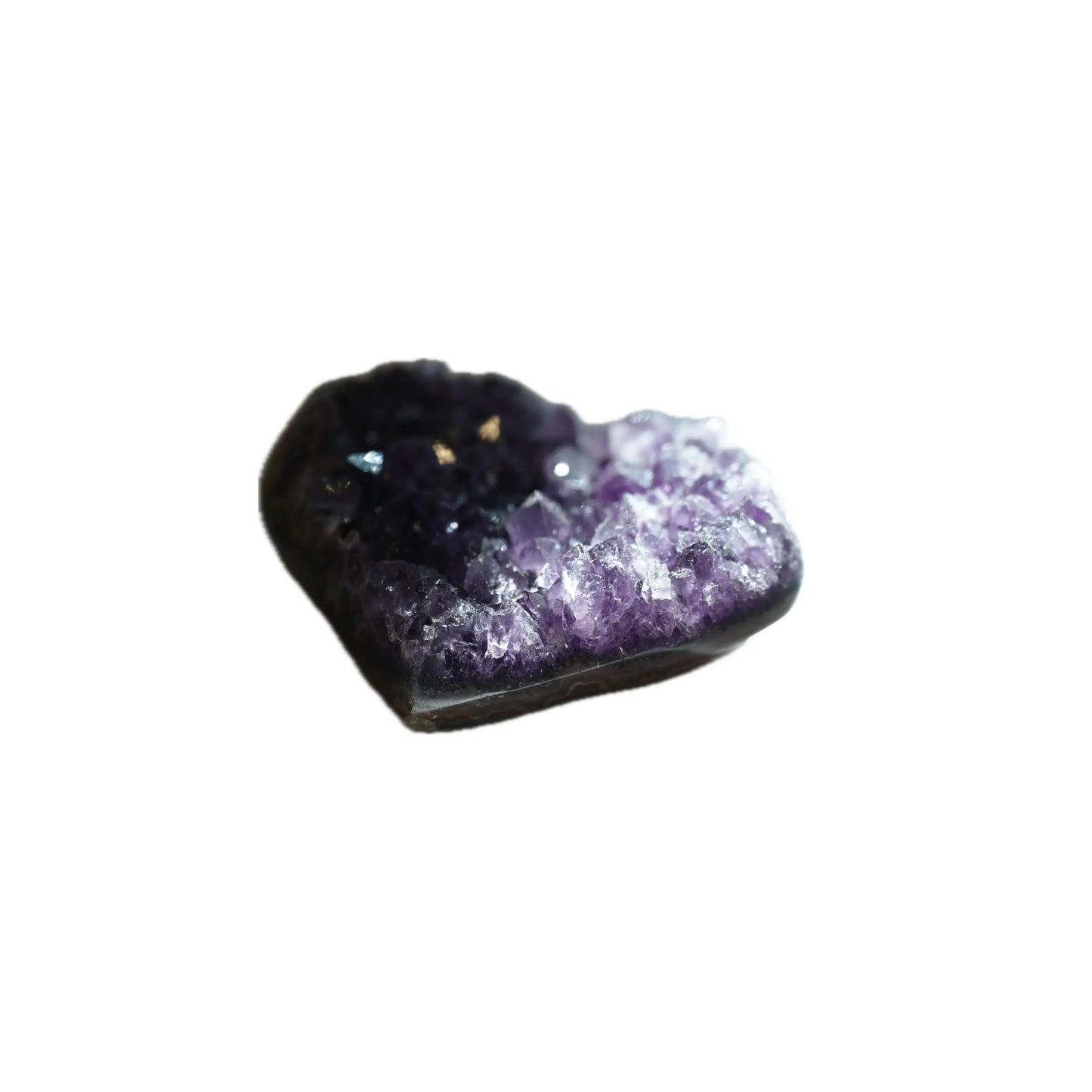 A slightly angled profile view of the same heart-shaped Amethyst crystal geode, emphasizing its depth and organic form. Natural light dramatically illuminates the sparkling purple and clear crystalline formations in the right foreground, while the background remains grounded in shadow, curated for manifestation and grounding by Singoau.