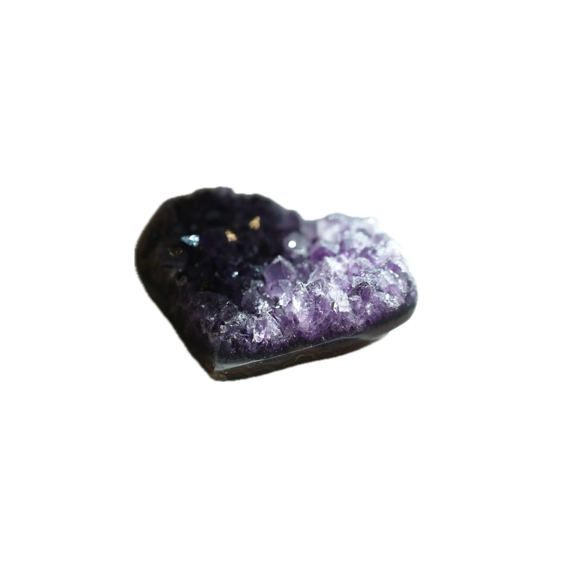 A slightly angled profile view of the same heart-shaped Amethyst crystal geode, emphasizing its depth and organic form. Natural light dramatically illuminates the sparkling purple and clear crystalline formations in the right foreground, while the background remains grounded in shadow, curated for manifestation and grounding by Singoau.
