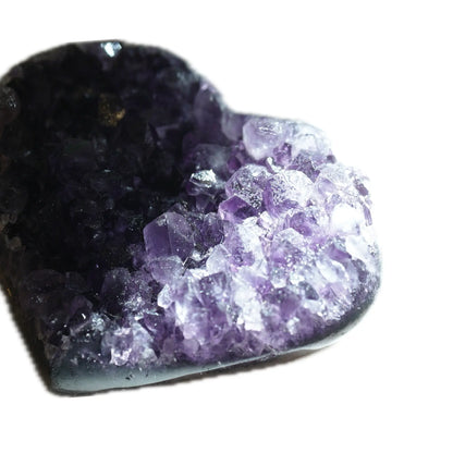 A macro, extreme close-up of the lit facets on the heart-shaped Amethyst geode cluster. This detailed shot captures the intricate, raw, and handpicked quality of the purple crystals, highlighting the unique imperfections that embody Singoau's Wabi-Sabi aesthetic for mindful ritual and sacred spaces.
