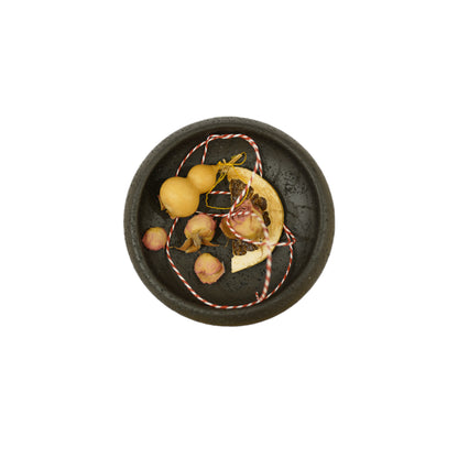 A minimalist, dark gray ceramic bowl on three wooden legs, featuring a slender stick protruding from the center.