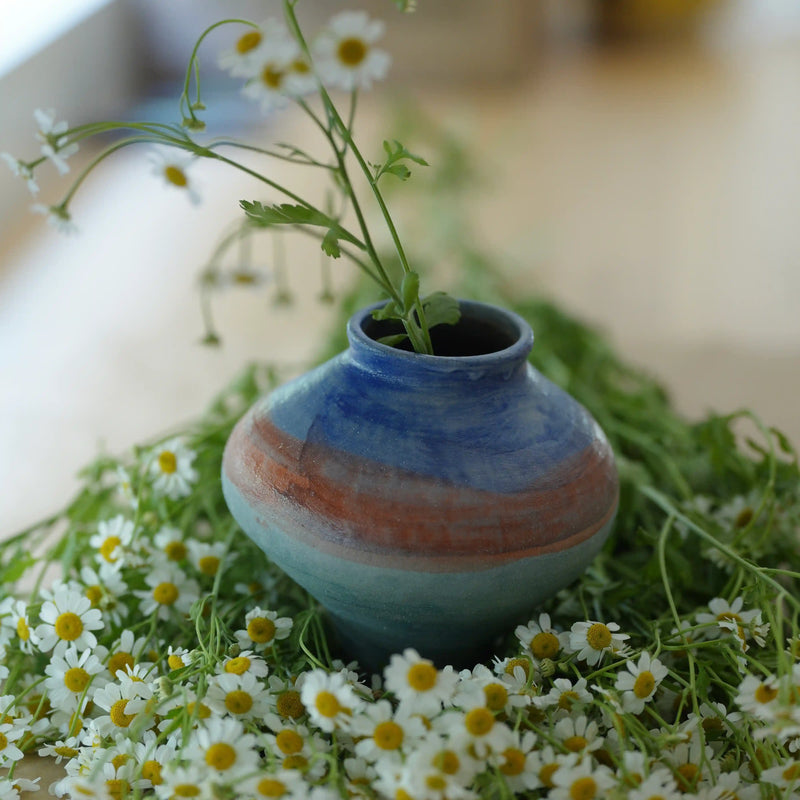 Handcrafted ceramic vase with blue and earth-tone glaze holding wild chamomile flowers in a wabi-sabi setting