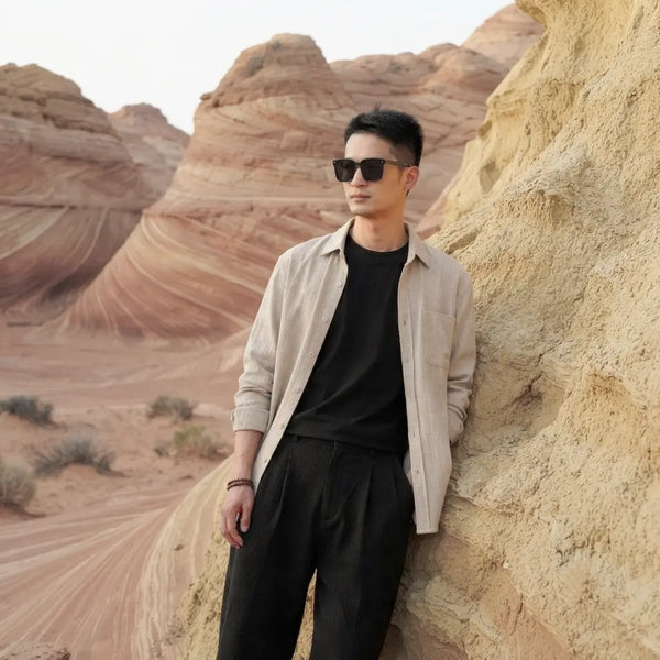 Man wearing sunglasses and casual clothes leaning against textured sandstone rock formations in a desert landscape.