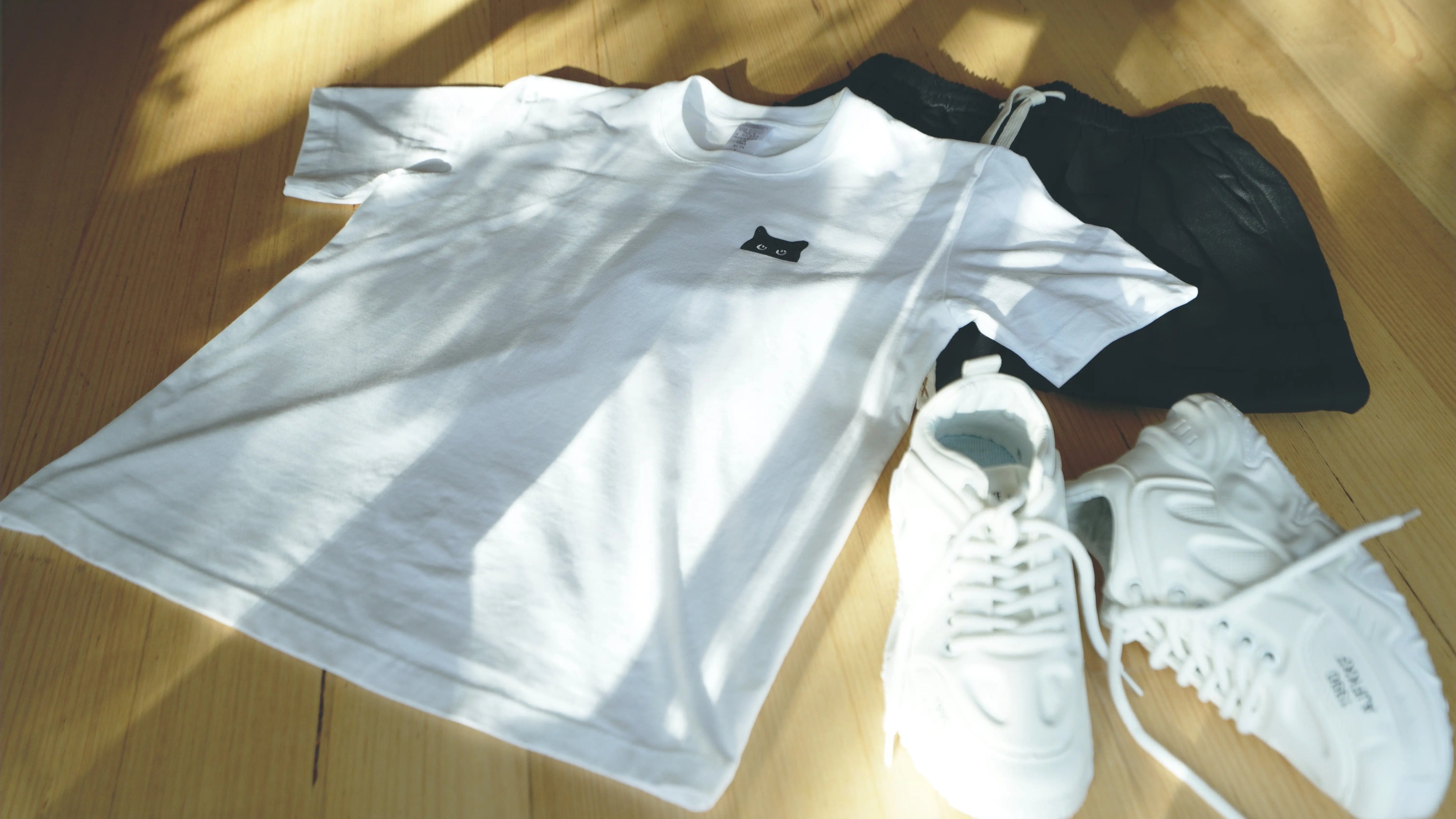 Flat lay of Singoau white cat print t-shirt, black casual shorts, and chunky white dad sneakers – minimalist summer fashion essentials for men and women at Singoau